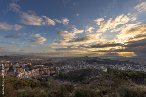 Picturesque landscape of Barcelona from the hill in the early morning. Sunbeams through the clouds. Dramatic sky over the city. Autumn in Barcelona  Spain.