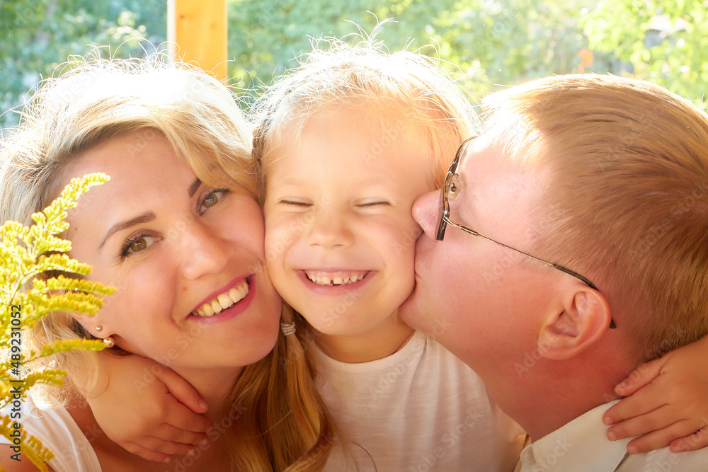 Portrait of Little blonde girl, mother and father on wooden terrace on nature or in the village and a green landscape in the background on a summer or autumn sunny day. Concept happy family Portrait of Little blonde girl, mother and father on wooden terrace on nature or in the village and a green landscape in the background on a summer or autumn sunny day. Concept happy family