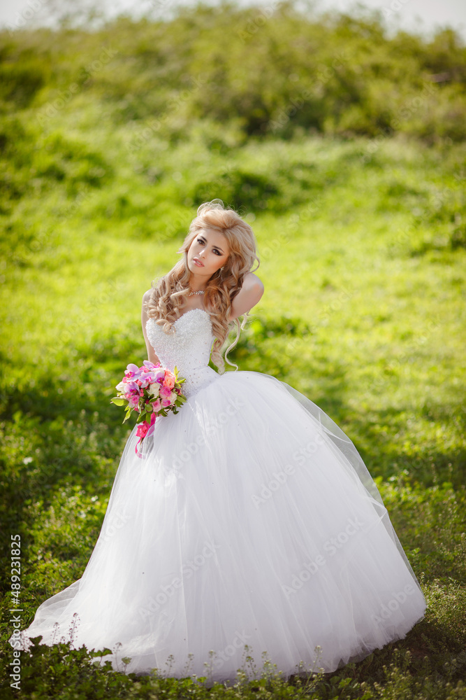 A beautiful blonde bride with a cool make-up in a wedding dress holds a bridal bouquet against the backdrop of a beautiful, green nature. Husband and wife, happy together, just married, newlyweds. A beautiful blonde bride with a cool make-up in a wedding dress holds a bridal bouquet against the backdrop of a beautiful, green nature. Husband and wife, happy together, just married, newlyweds.