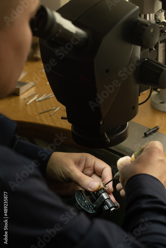 Professional jeweler at work. The jeweler looks into the microscope and decorating precious ring with beautiful gemstones.