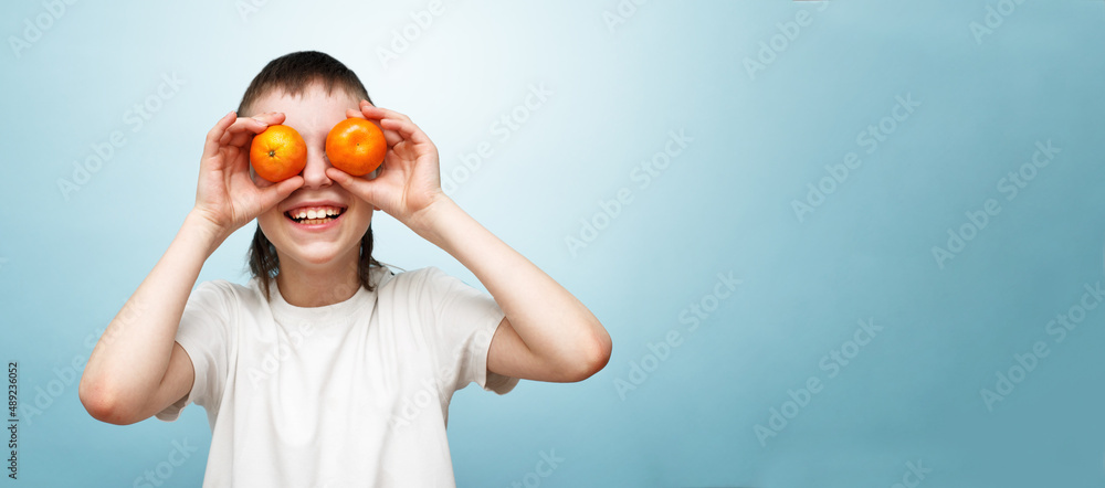 happy smiling boy with two mandarins covering his eyes on blue background. happy smiling boy with two mandarins covering his eyes on blue background.