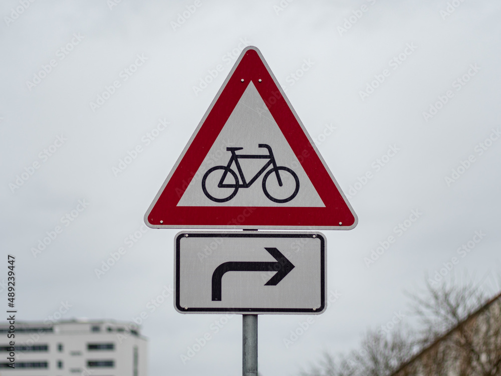 Cyclists warning street sign with an arrow to the right. Road sign to pay attention to bicycle riders in a city. Symbol in front of an overcast sky. Caution when being part of the traffic. Cyclists warning street sign with an arrow to the right. Road sign to pay attention to bicycle riders in a city. Symbol in front of an overcast sky. Caution when being part of the traffic.