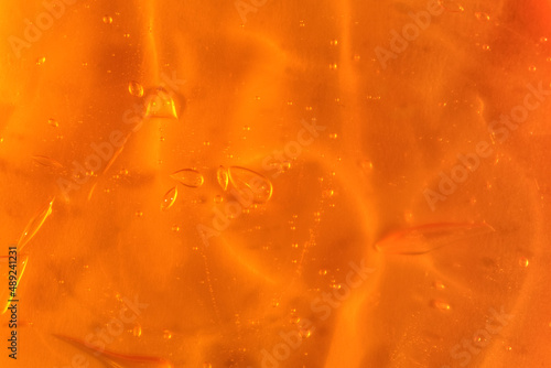 Texture of transparent yellow gel with air bubbles and waves on orange background. Concept of skin moisturizing, body care and prevention of covid19. Liquid beauty product closeup. Backdrop, flat lay