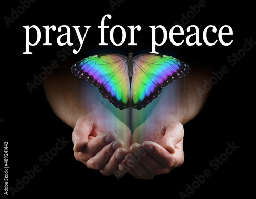 Pray for Peace Butterfly Release Concept - male cupped hands emerging from black background with a beautiful multicoloured butterfly rising up and the words pray for peace above
