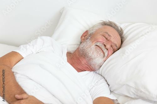 Senior retirement man sleeping happily in his white blanket bed in bedroom