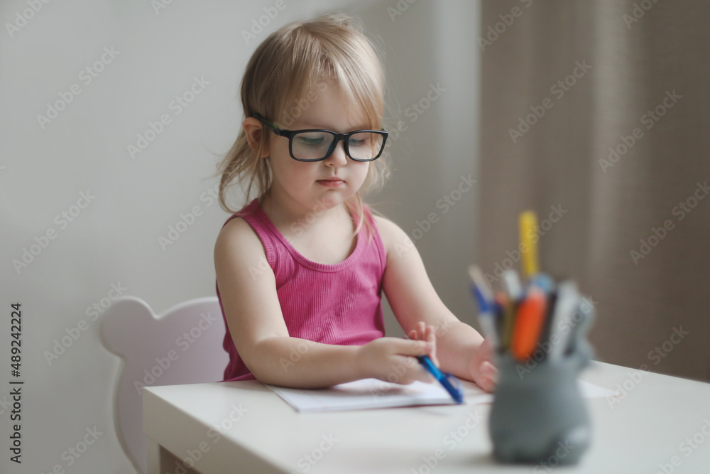 small funny girl in eyeglasses writing and drawing at the table small funny girl in eyeglasses writing and drawing at the table
