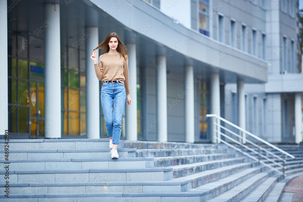 young woman in jeans and a sweater walks around the city on a summer day.