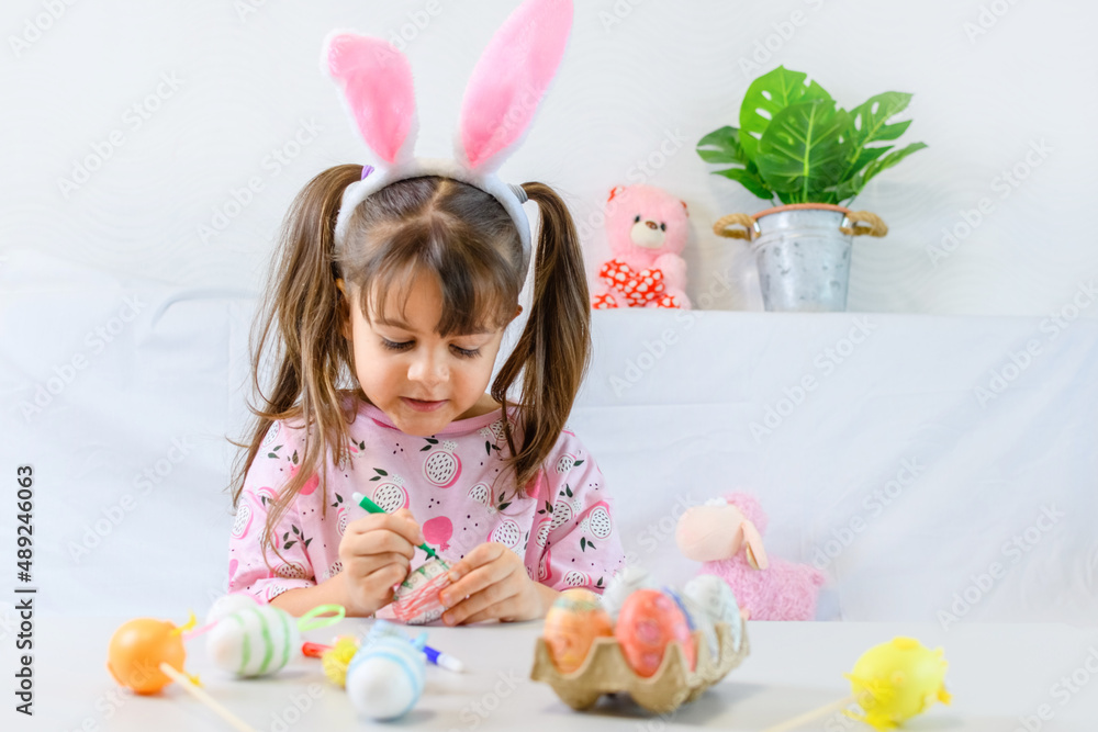 Happy little girl with bunny ears painting the egg with fiberpen, preparing for Happy Easter day. Preparing handmade .