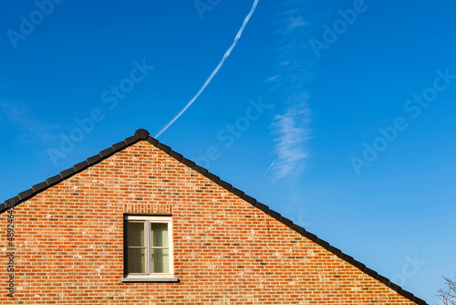 Gabled roof old brick house in Gavere town With jet smoke trail in the background sky. Gavere is located in the Belgian province of east flanders, Belgium photo