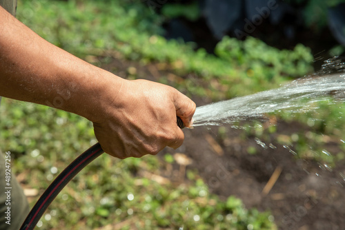 Hand holds the rubber hose by pressing the hole with the thumb to spray water in the garden, housework. © Harold