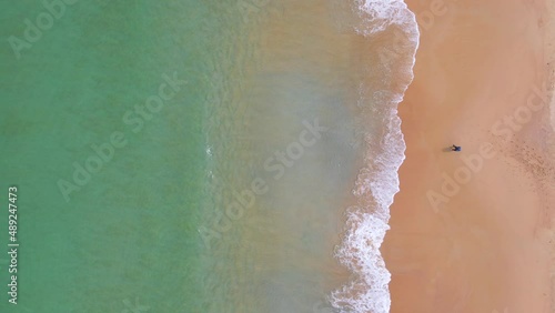 Aerial view of ocean wave reaching the coastline with a man fishing. Beautiful tropical beach from top view. Andaman sea in Thailand. Summer holiday vacation concept. 4K drone video