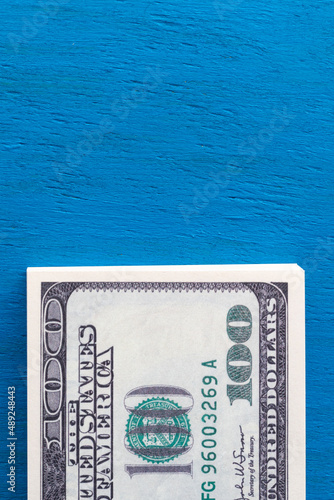 Vertical photo of a stack of hundred-dollar bills on a blue background with copy space. A wad of money on the table.