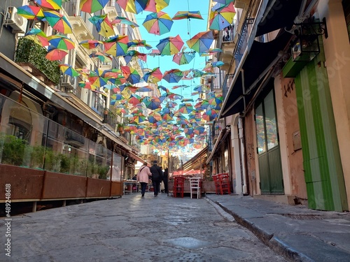 Stradina caratteristica in basolato del centro di Catania, con decorazioni con ombrelli colorati appesi tra i palazzi antichi, e persone che camminano photo