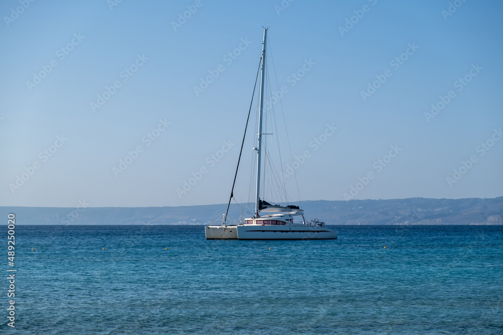 Sailing boat catamaran anchored at rippled sea, Land and blue sky background