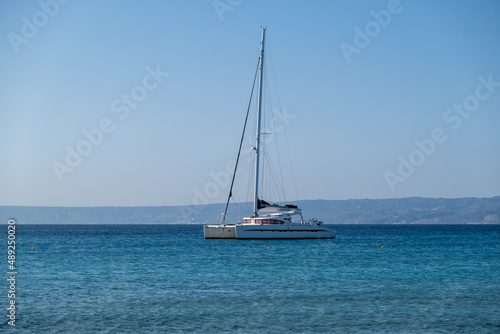 Sailing boat catamaran anchored at rippled sea, Land and blue sky background