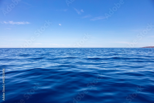 Ocean sea water surface deep blue, calm with ripple, small cloud on blue sky background,