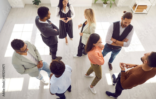 Group of diverse people communicating at business event. Smiling multi ethnic employees talking while standing in office at casual meeting or psychological training session. High angle shot from above photo
