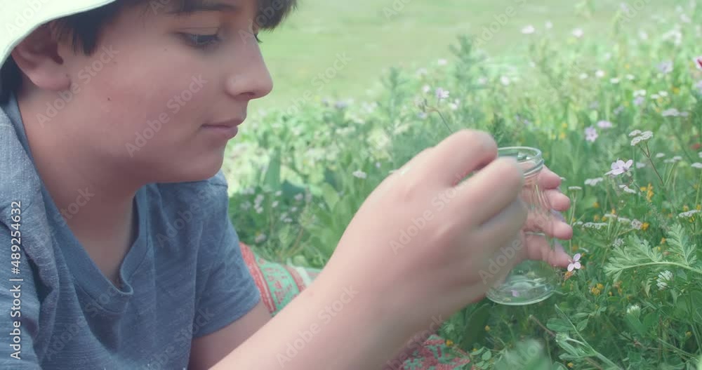 The boy collects plants with tweezers and puts them in a jar.Biology project for the summer holidays
