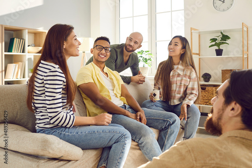 Happy multiethnic friends sit on couch gather at home have fun chatting talking together. Smiling diverse international young people or colleagues speak share ideas relax on weekend. Diversity. photo