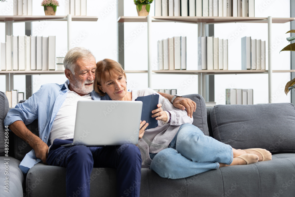 senior couple using laptop computer and tablet on sofa senior couple using laptop computer and tablet on sofa