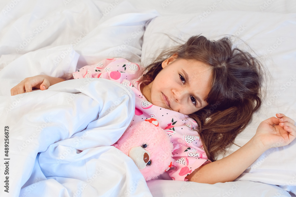 Angry dark hair girl sleeping sweetly in the morning on wihte bed linens at home. Childrens dreams, comfort
