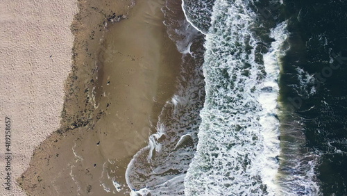 Aerial drone view flight over sea waves that roll onto sandy shore. Top view. Waves with white foam hit sandy shore. Nature, natural background. Concept eco, environment, climate change, traveling