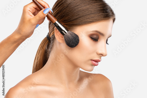Portrait of a beautiful brunette girl with beautiful fresh makeup and healthy clean skin.Makeup artist holds a powder brush in her hands. Professional makeup concept
