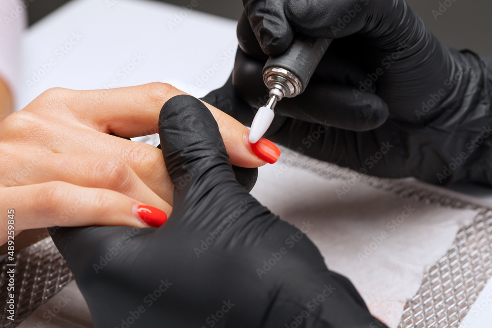 The master of the manicure saws and attaches a nail shape during the procedure of nail extensions in the beauty salon. Professional care for hands.
