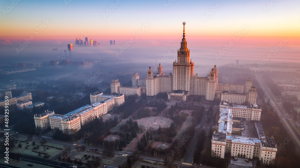 Fototapeta premium Aerial view of Moscow State University on a foggy day. Amazing sun rise. Moscow City trade and business center is covered with fog