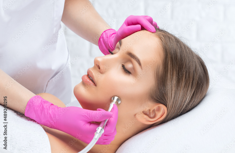 Cosmetologist makes procedure microdermabrasion on the face against acne and blackheads near the eyes. Women's cosmetology in the beauty salon. Cosmetologist makes procedure microdermabrasion on the face against acne and blackheads near the eyes. Women's cosmetology in the beauty salon.