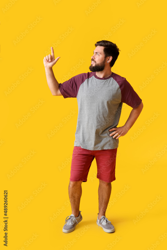Handsome man in t-shirt pointing at something on yellow background
