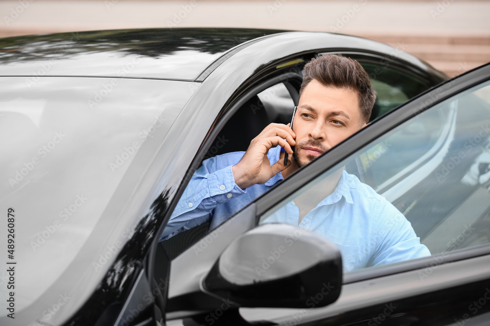 Handsome businessman talking by mobile phone in modern car