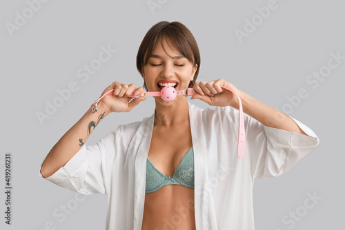 Tableau sur toile Beautiful young woman with mouth gag on grey background