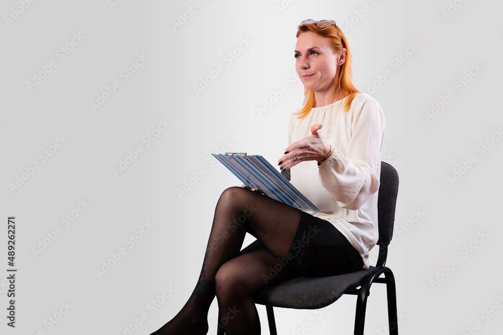 A girl, in a white blouse, sits on a chair with a folder in her hands, on a gray background A girl, in a white blouse, sits on a chair with a folder in her hands, on a gray background