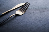 Gold spoon, fork, knife and clean empty black plate. Set of stylish black and gold cutlery on black background. Fashionable and luxury eating. Top view. Copy space for your text.