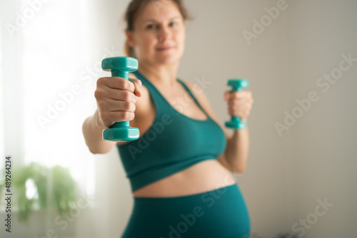 A pregnant woman is exercising with dumbbells. Concept of a healthy lifestyle during pregnancy. Sports activities before the birth of baby. Useful exercises, fitness for health of the expectant mother