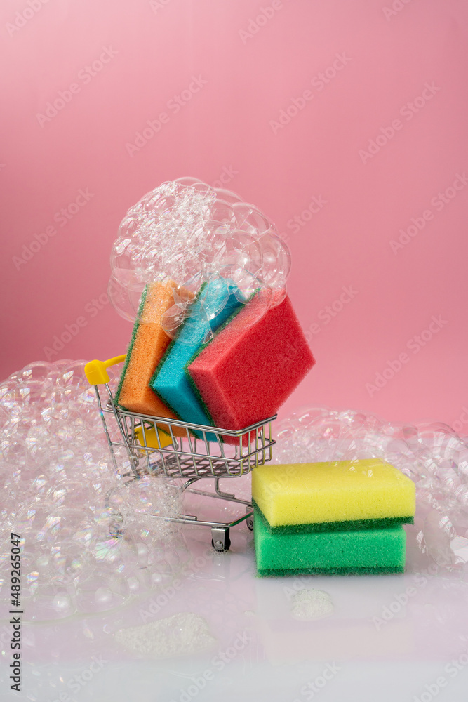 sponges for washing dishes in foam in a trolley on a pink background