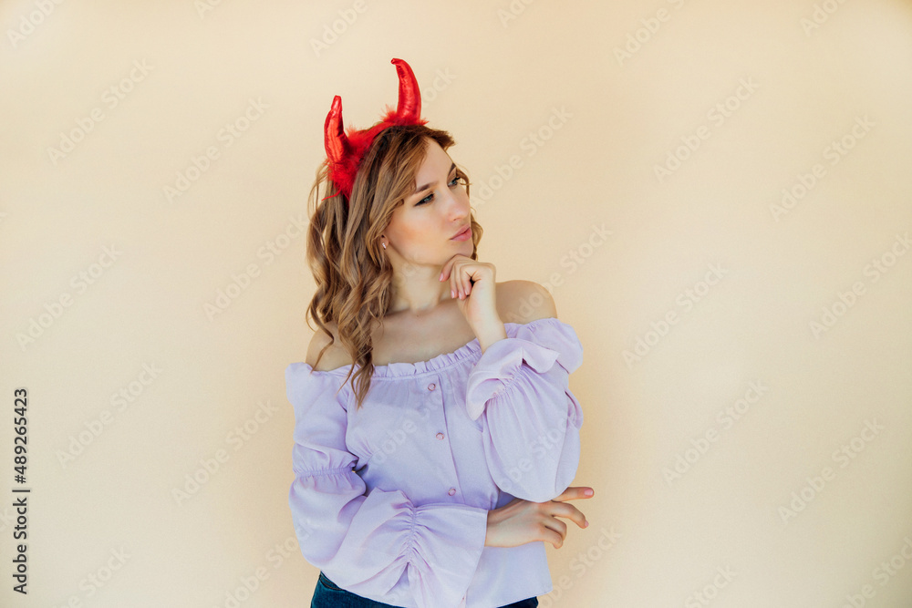 Portrait of a girl with wavy hair, in a devil costume for Halloween near a beige wall. Portrait of a girl with wavy hair, in a devil costume for Halloween near a beige wall.