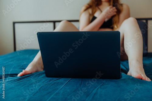 Webcam model. Young sexy woman using laptop on the bed. Flirting, online sex-chat, nudes concept. photo