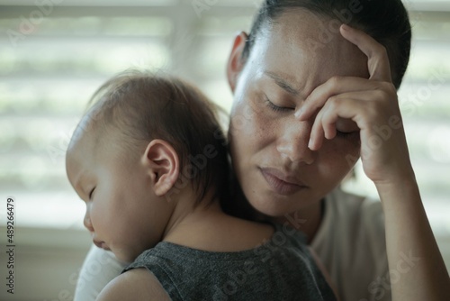 A depressed worried woman at home holding her baby. Parenting difficulties.