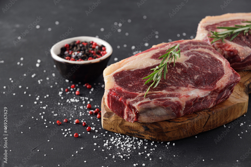 Raw beef steak on a cutting board with rosemary and spices.