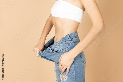 Fit woman having ripped jeans and white bra on stretching jeans to show belly after weight loss. Keeping diet and exercising. Aiming for improving health and getting fit.