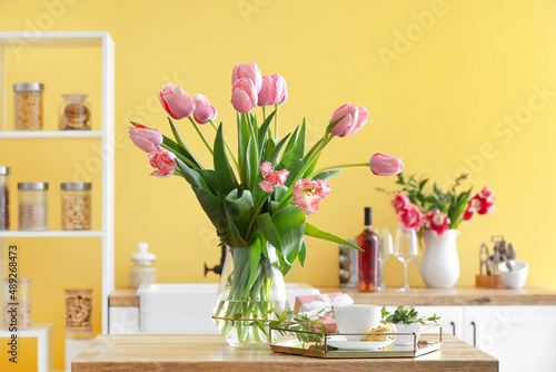Vase with tulips, gift box, cup of coffee and macarons on table in kitchen