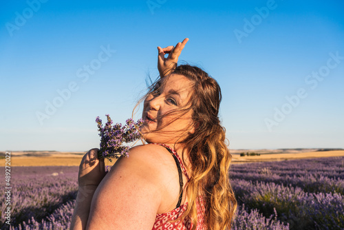 beautiful and happy plus size woman looking at camera holding lavender flowers.