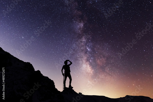 Silhouette of a person on the top of mountain in starry night sky. Bright milky way galaxy behind him.