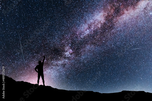 Silhouette of a person stands on the hill in starry night sky. Bright milky way galaxy behind him.