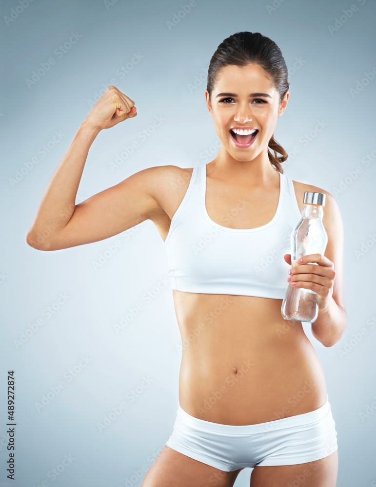Itll be worth it once you reach your goal. Studio portrait of an attractive young woman cheering while holding a water bottle against a grey background. Itll be worth it once you reach your goal. Studio portrait of an attractive young woman cheering while holding a water bottle against a grey background.