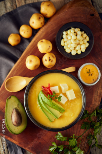 Ecuadorian locro de papa a traditional potato and cheese soup served with avocado and hominy. It’s on a wooden background