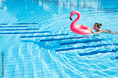 Pool party girl. Young sexy woman with pink flamingo in bikini swimsuit float in blue pool water. Resort spa in hotel on travel holidays vacation.