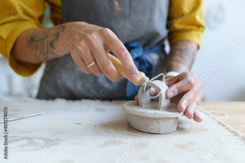 Hands of female artisan working with raw clay in pottery studio. Young student girl or master preparing material for shaping ceramic kitchenware and modeling jar. Pottery business and workshop concept